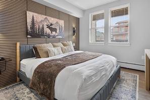Een slaapkamer met een bed, een hangend kunstwerk, een raam en een telefoon aan de muur.