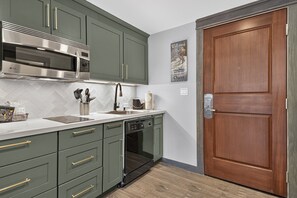 Een keuken met een ingebouwde magnetron, een roestvrijstalen afzuigkap en een vaatwasser. Er is een houten deur en een aan de muur bevestigd schilderij.