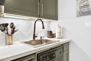 A kitchen with a stainless steel sink, a dish soap dispenser, and a set of kitchen utensils in a metal container. - Premium Unit 4573 -1br Kitchenette Founders Pointe 1 Bedroom Condo (Winter Park)