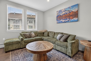 A living room with a sectional sofa, a round coffee table, and a painting of a mountain landscape. - Premium Unit 4573 -1br Kitchenette Founders Pointe 1 Bedroom Condo (Winter Park)