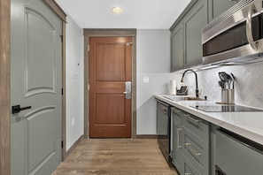 A narrow kitchen with a wooden door, stainless steel appliances, and a tiled backsplash. - Premium Unit 4571 - Studio - Founders Pointe Condo (Winter Park)