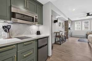 A modern kitchen with built-in appliances, a dining area with a bar stool, and a living room with a sofa and a fireplace. - Premium Unit 4571 - Studio - Founders Pointe Condo (Winter Park)