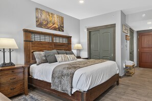 A bedroom with a wooden bed, two bedside tables with lamps, a large painting on the wall, and a green door. - Premium Unit 4571 - Studio - Founders Pointe Condo (Winter Park)