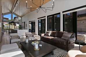 A modern living room with a leather sofa, a coffee table with decorative items, and large windows offering a view of the outdoors. - 4br Deer Valley Home With Hot Tub, Sauna & Views 4 Bedroom Home (Heber City)