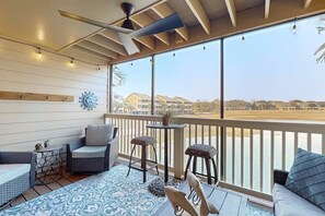 Varanda com vista para a praia, ventilador de teto e mesa com planta.