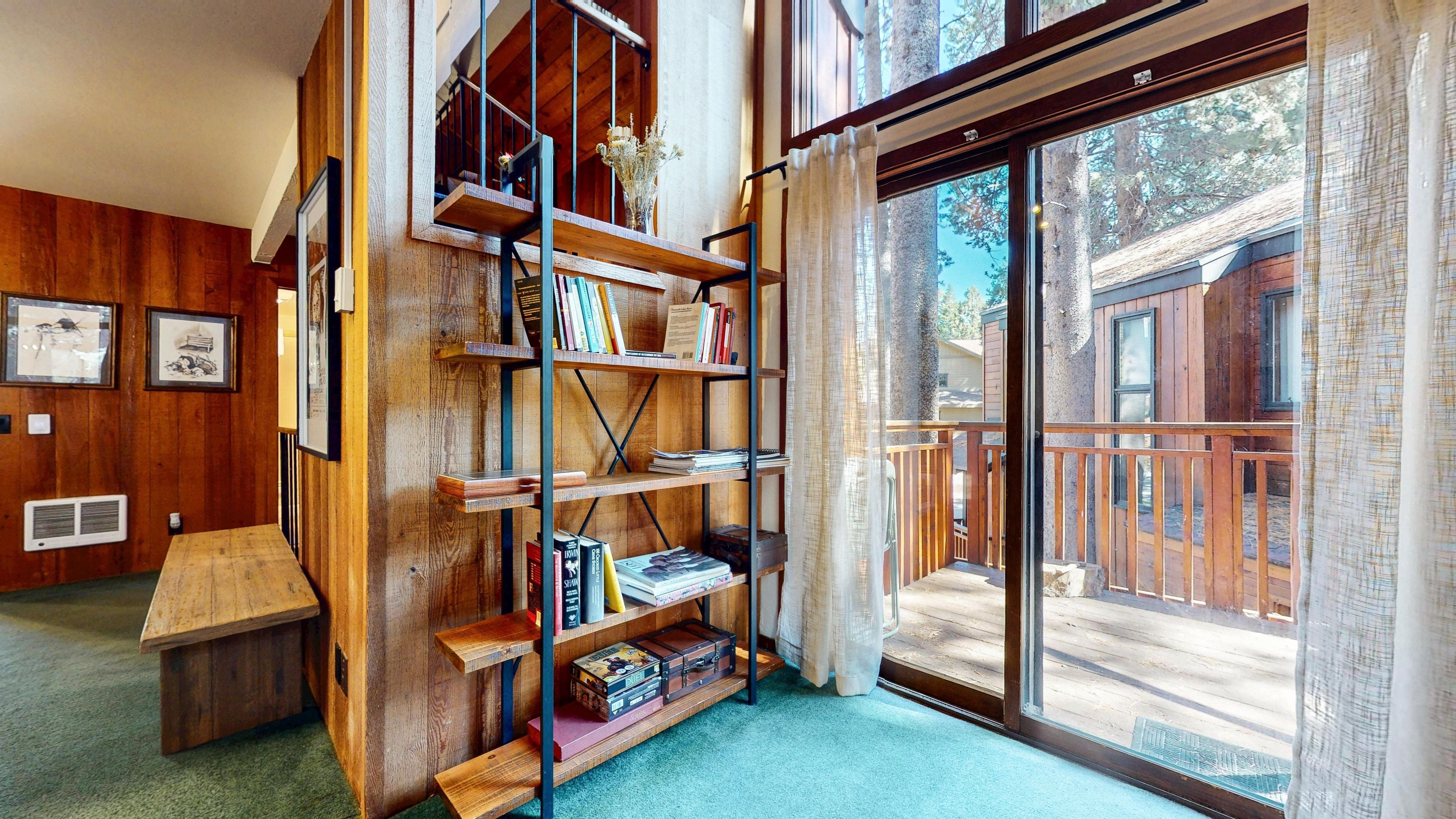 Een kamer met een houten boekenkast, een kleine tafel en een grote schuifdeur die leidt naar een terras.