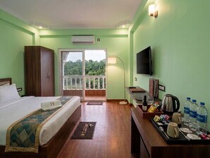 A hotel room with a bed, a television, a balcony with a view of greenery, and a tray with breakfast items.