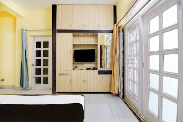 A room with a bed, a TV, a desk, and a large window. - Super Collection O Jyotirindra Nandi (Kolkata)