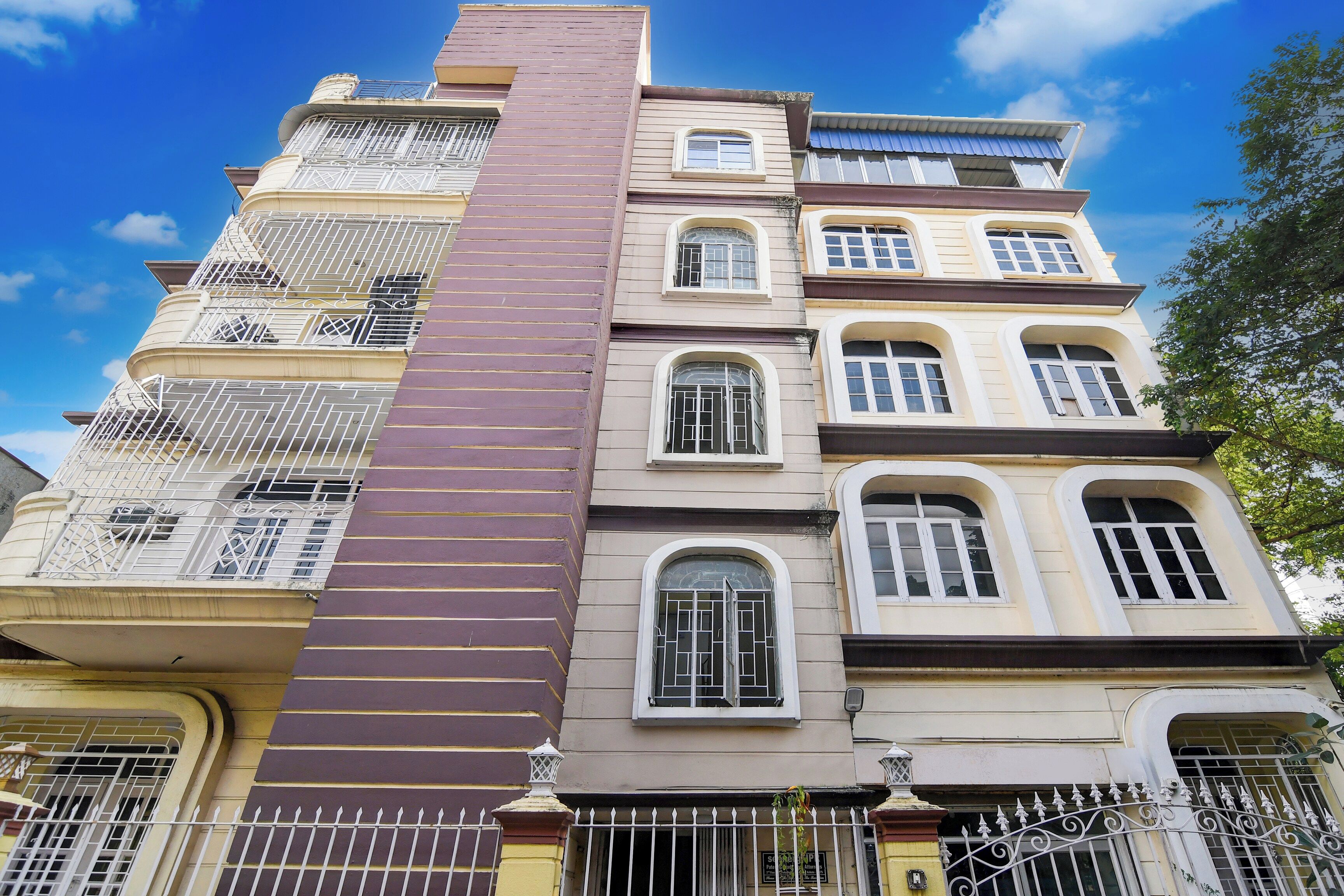 A multi-story building with balconies, a central vertical structure, and a gated entrance.