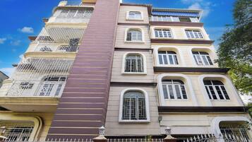 A multi-story building with balconies, a central vertical structure, and a gated entrance.
