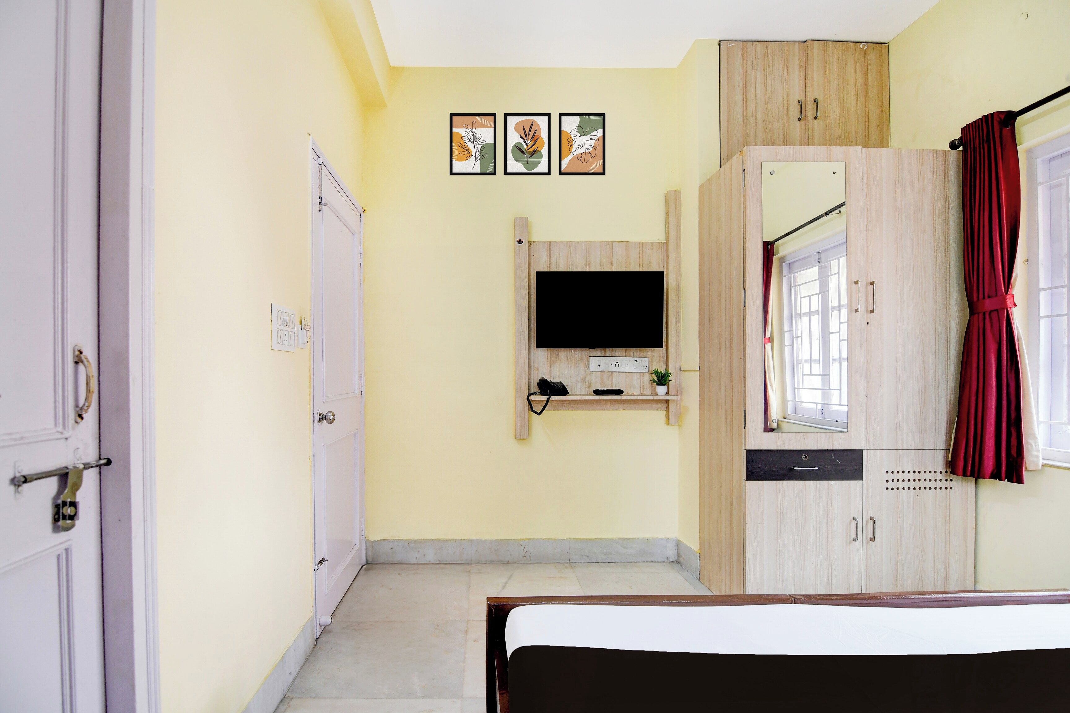 A bedroom with a bed, a wardrobe, a television, and a window with curtains.
