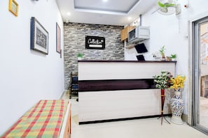 A reception desk with a stone wall backdrop, a sign indicating company service, and a colorful checkered bench. - Super Collection O Jyotirindra Nandi (Kolkata)