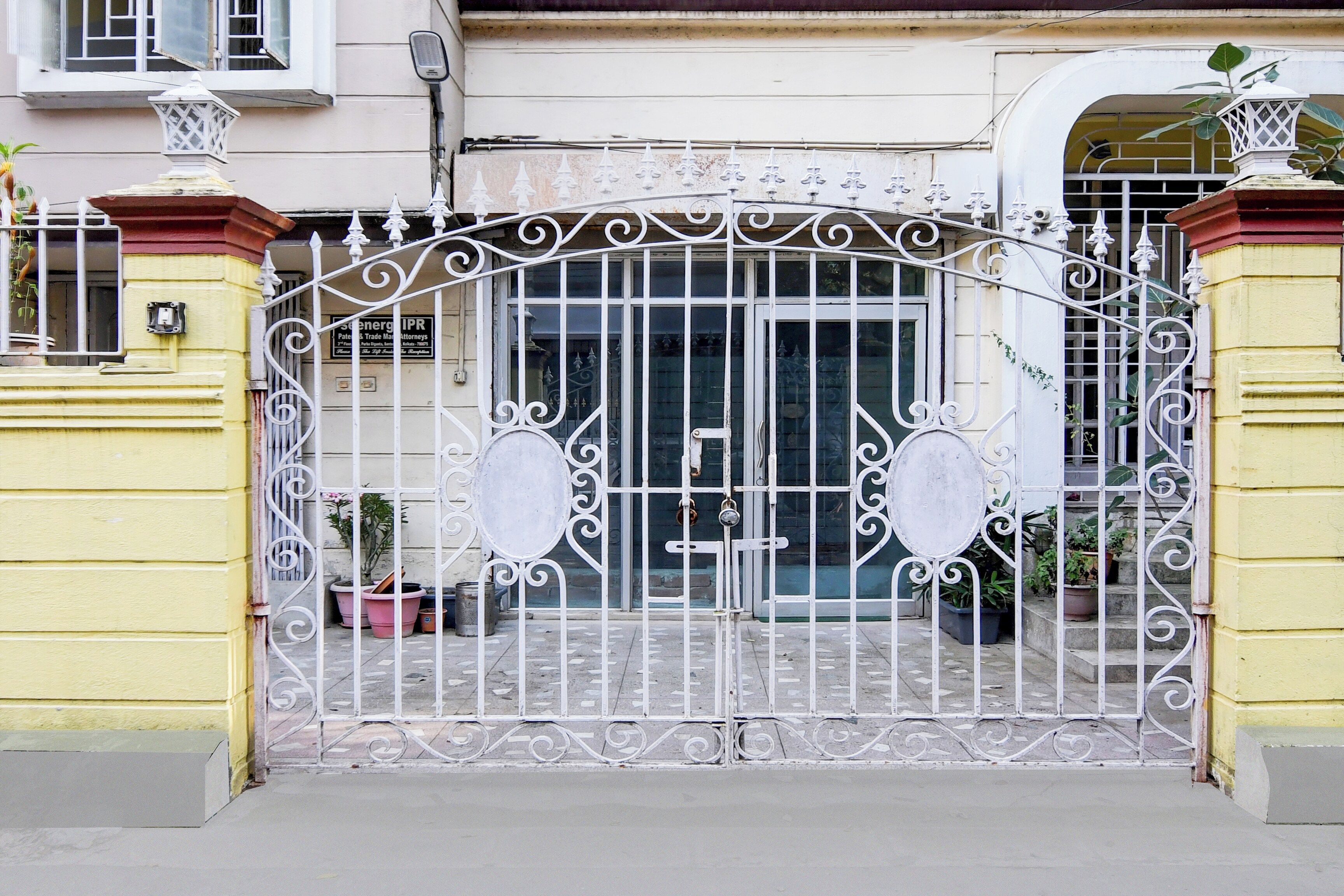 A gated entrance with a metal gate featuring decorative scrollwork and two circular signs.