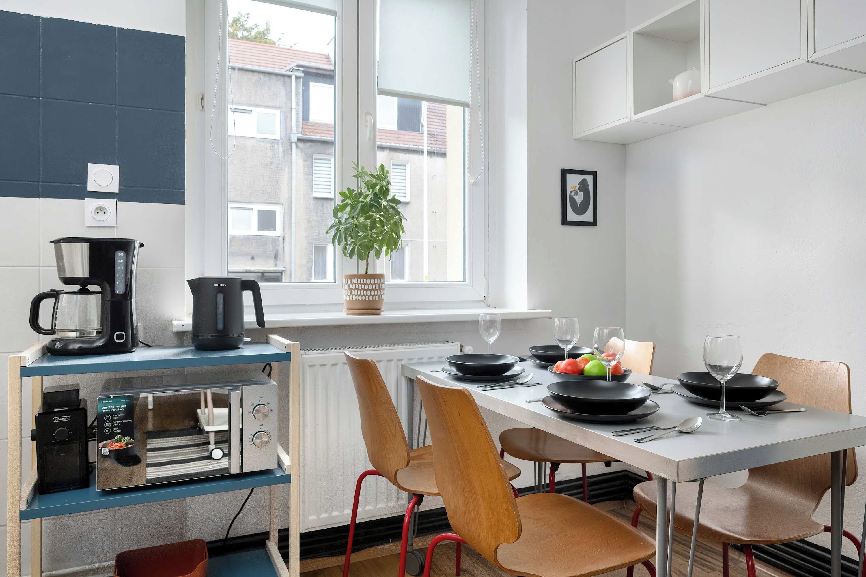 Een moderne keuken met een eettafel voor twee personen, een koffiezetapparaat, een waterkoker en een plant in een pot bij het raam.