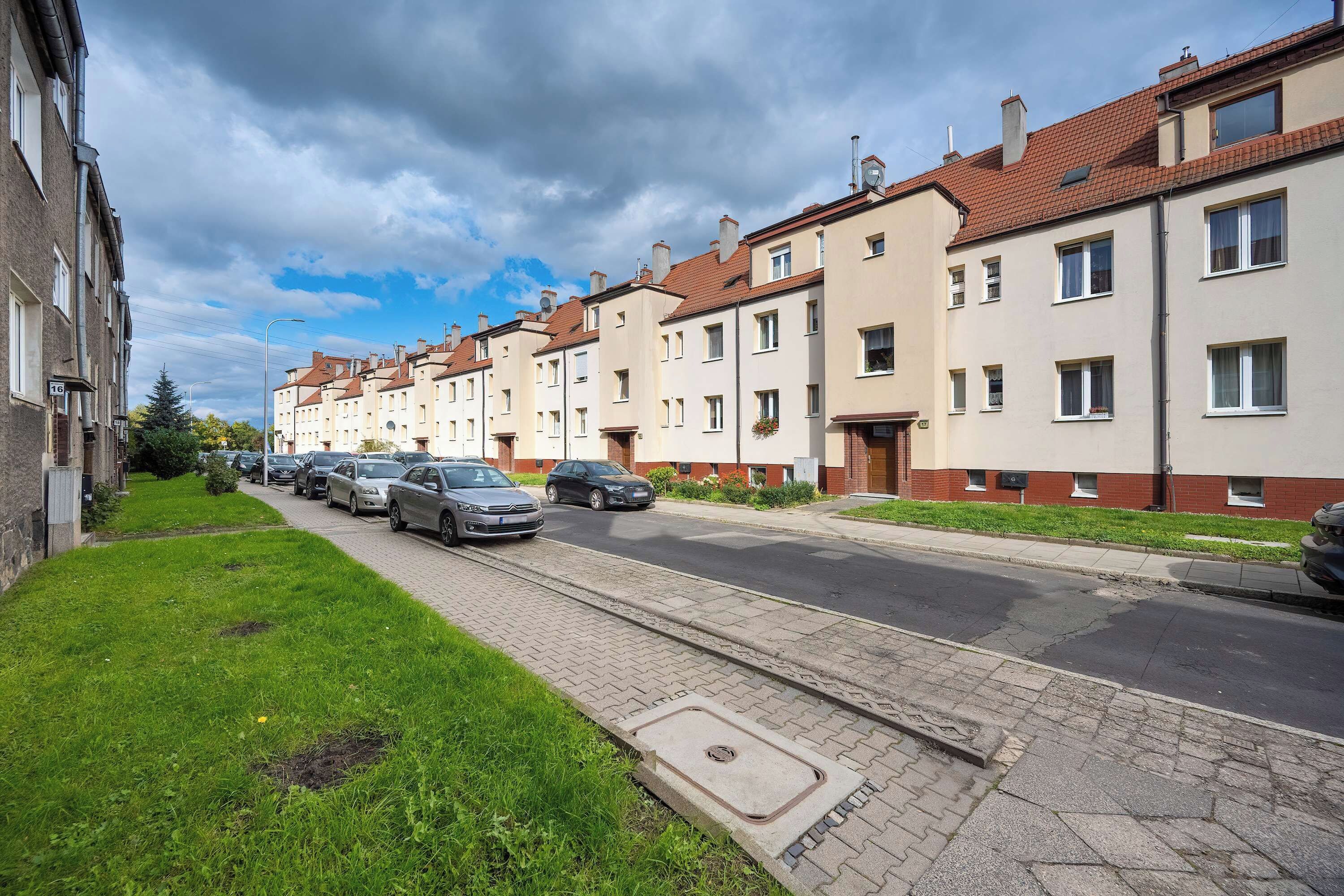 A residential street with townhouses, parked cars, and a grassy area.