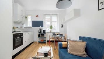 Ein kompakter Wohnbereich mit Küchenzeile, Essplatz und einem blauen Sofa mit Webdecke.