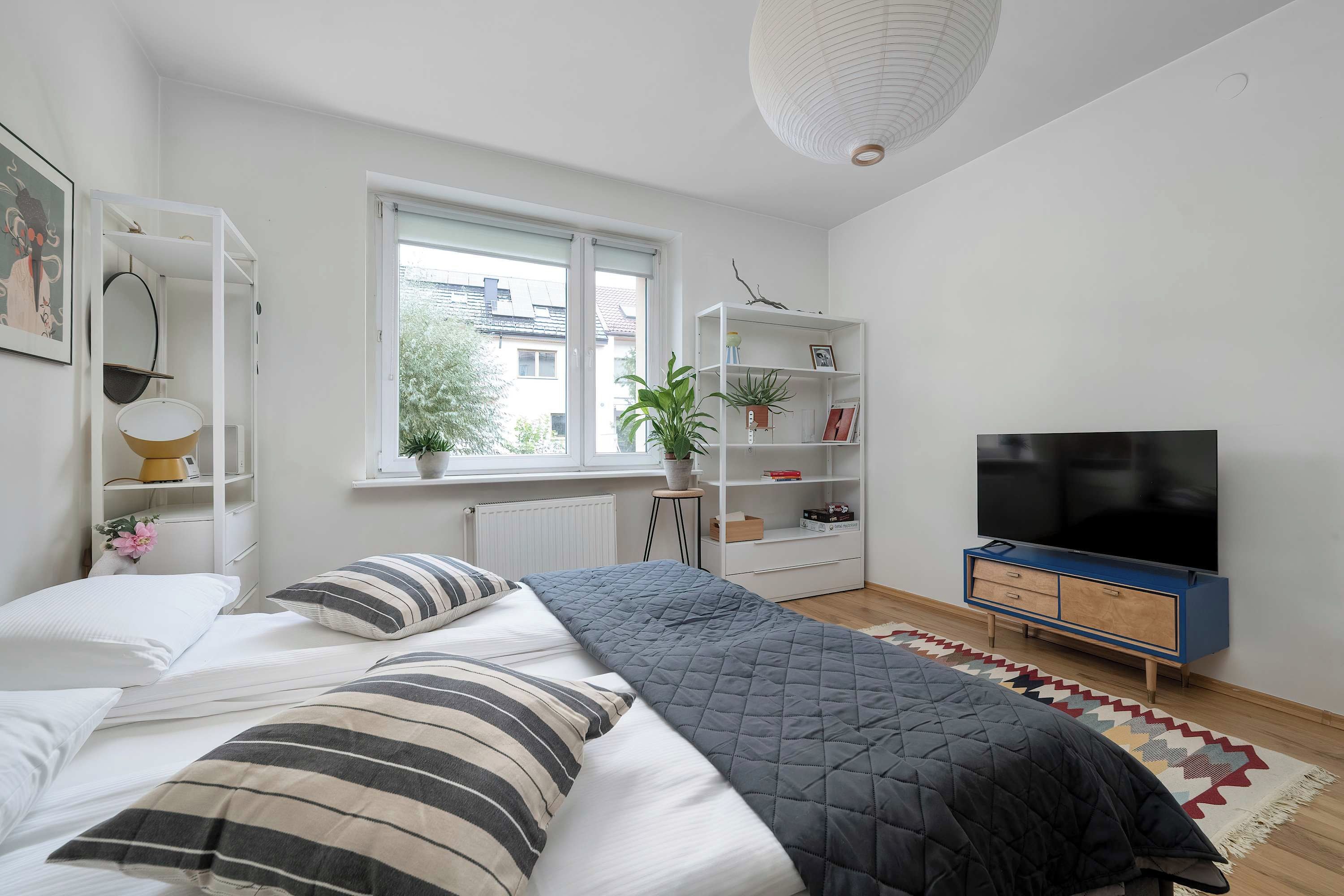 Een moderne slaapkamer met een bed, een televisie, een boekenkast en een raam.