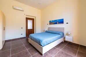 A bedroom with a bed, a nightstand, a wall-mounted painting, and a door. - Terrazza Lulu by Napoliapartments (Naples)
