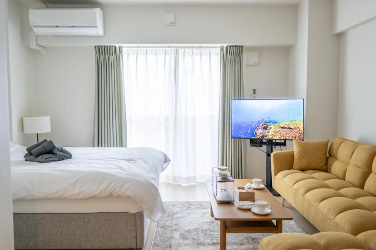 A hotel room with a bed, a sofa, a television, and a table with cups and a tissue box.