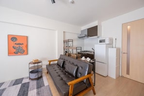A compact living space with a sofa, a kitchen area including a microwave and a refrigerator, and a small storage unit. - Hotel HIRAKU RYUKYU (nahashi)