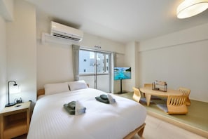 A hotel room with a bed, a TV, a dining table with chairs, and an air conditioning unit. - Hotel HIRAKU RYUKYU (nahashi)