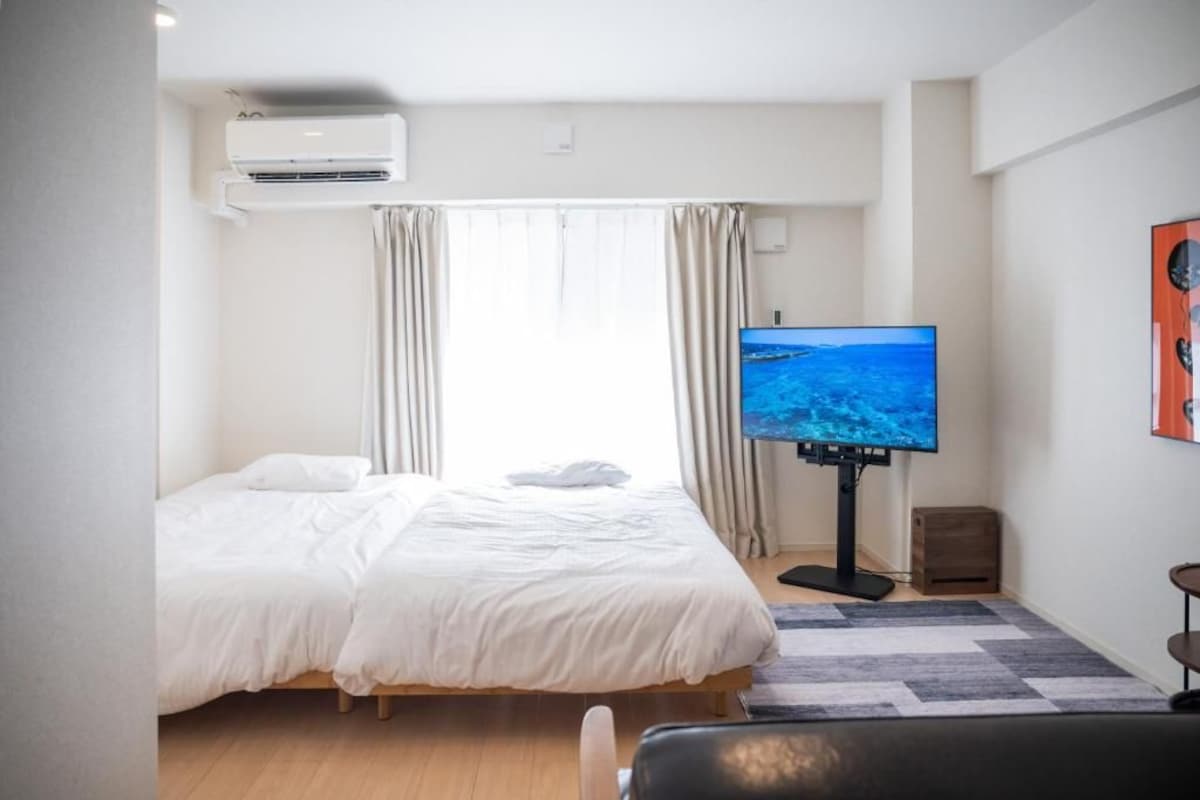 A hotel room with a bed, a television on a stand, an air conditioning unit, and a window with curtains.