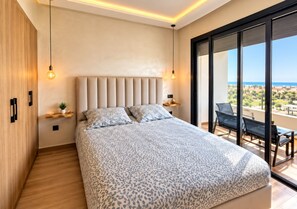 Une chambre moderne avec un grand lit, une vue sur l’extérieur et un balcon aménagé avec des sièges.