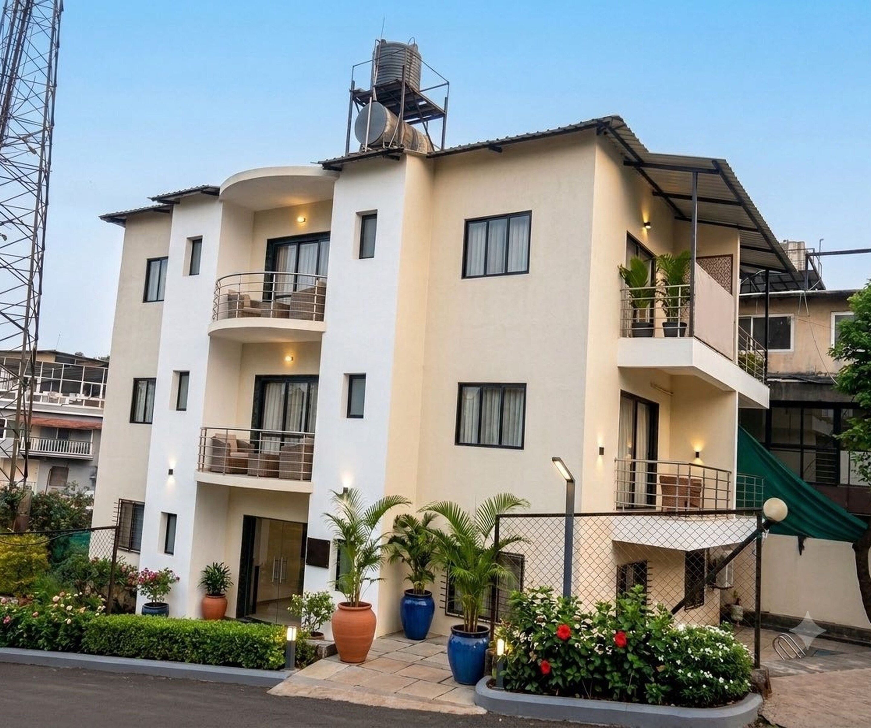 A multi-story hotel with balconies, a water tank on the roof, and potted plants in the foreground.