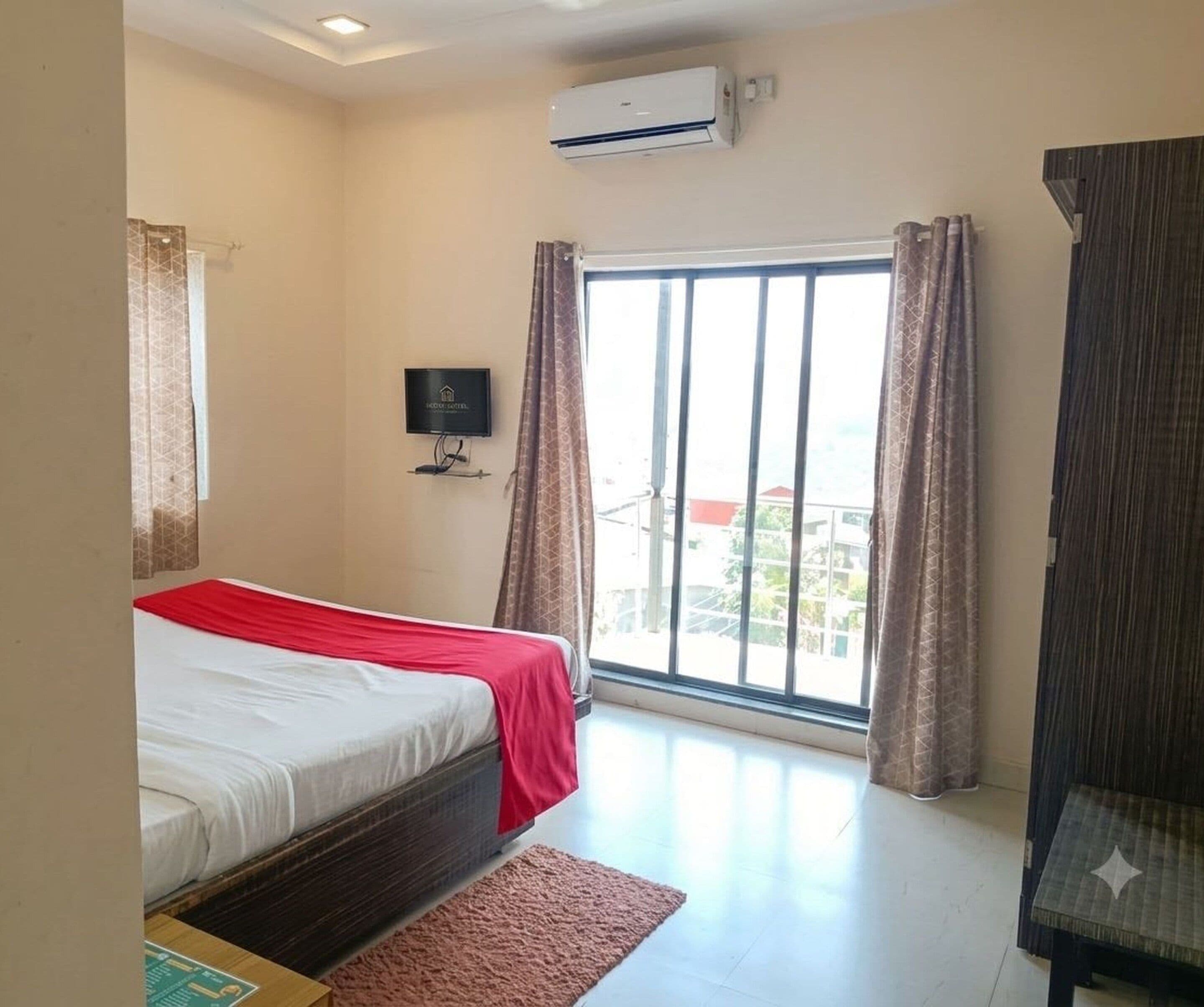 A hotel room with a bed, a TV, an air conditioner, and a view through a large window.