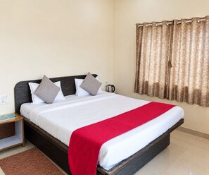 A neatly made bed with a red blanket, a dark headboard, and a window with patterned curtains. - Deluxe With Balcony Oraa Stay (Mahabaleshwar)