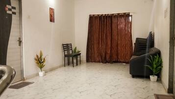 A room with a marble floor, a ceiling fan, a door with a checkered pattern, a brown curtain, a black sofa, and two potted plants.