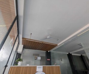 A reception desk with a wooden panel, a ceiling fan, and a security camera. - Luxury Hotel O 69 (Gurugram)