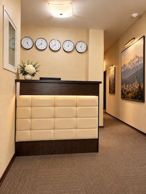 Een hotel receptie met een receptiebalie, meerdere wandklokken, een ingelijst beeld en een tapijtvloer.