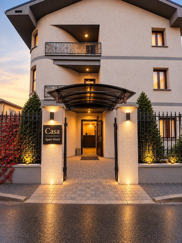 Una entrada de hotel moderna con un paseo techado, un letrero que indica que es un 'Apart Hotel' y un acceso mediante portón.
