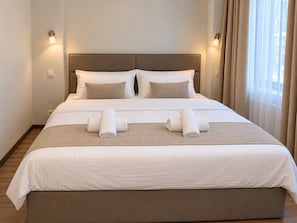 Een hotelkamer met een groot bed, twee kussens, een nachtkastje en een raam met gordijnen.