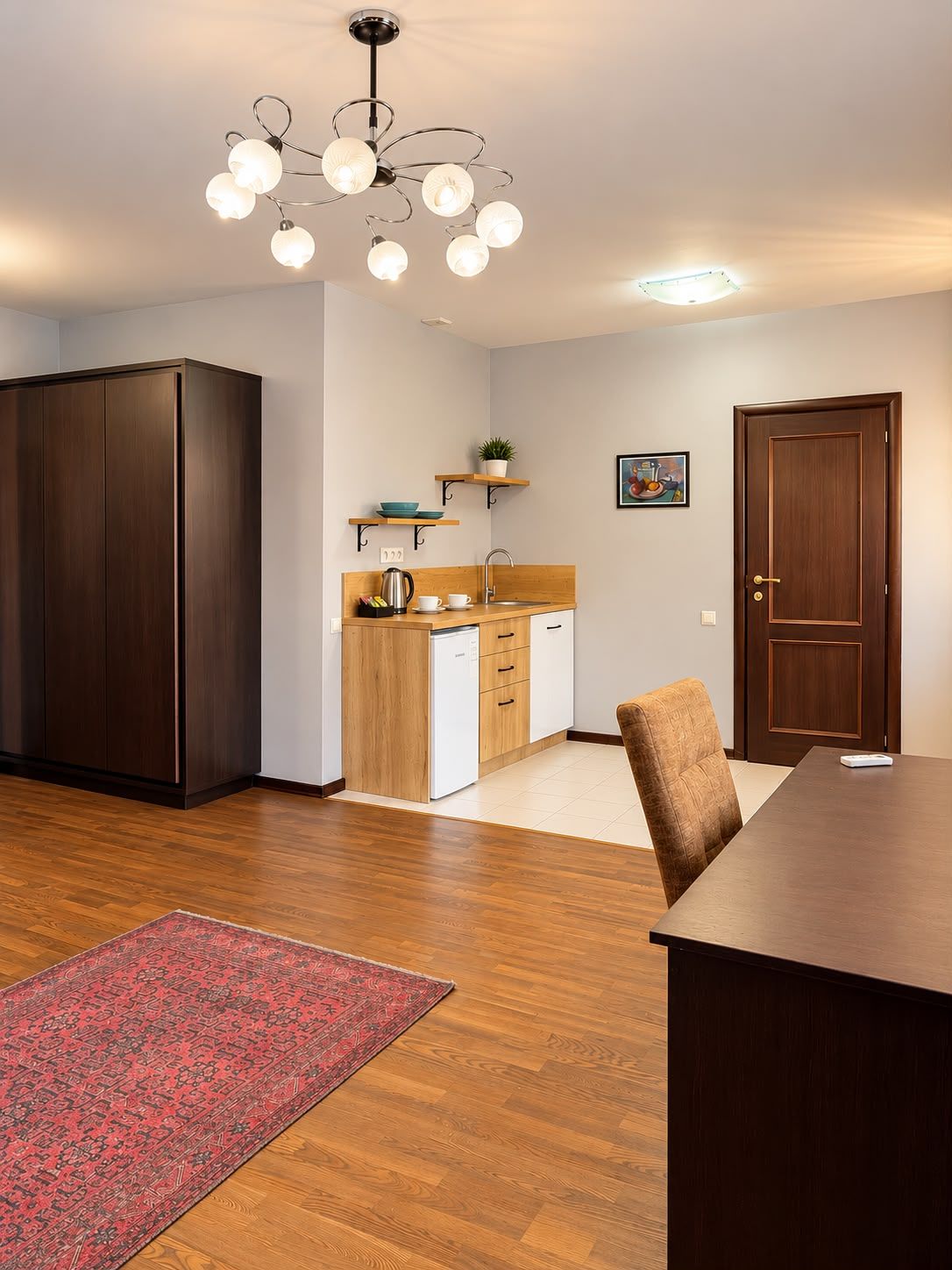 Una cocina compacta con lavavajillas integrado, una mesa de comedor de madera con sillas y un tapete rojo estampado.