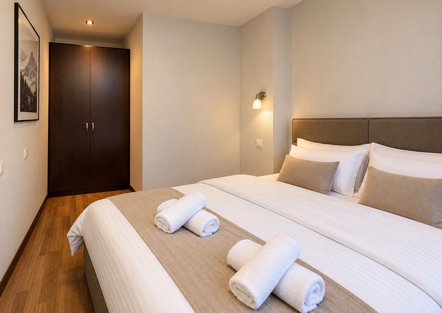 Hotellihuone, jossa on suuri sänky, vaatekaappi ja seinään kiinnitetty valaisin.
