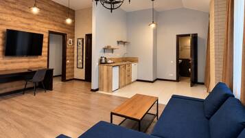 A modern living room with a blue sofa, a wooden coffee table, and a TV mounted on a wooden wall.
