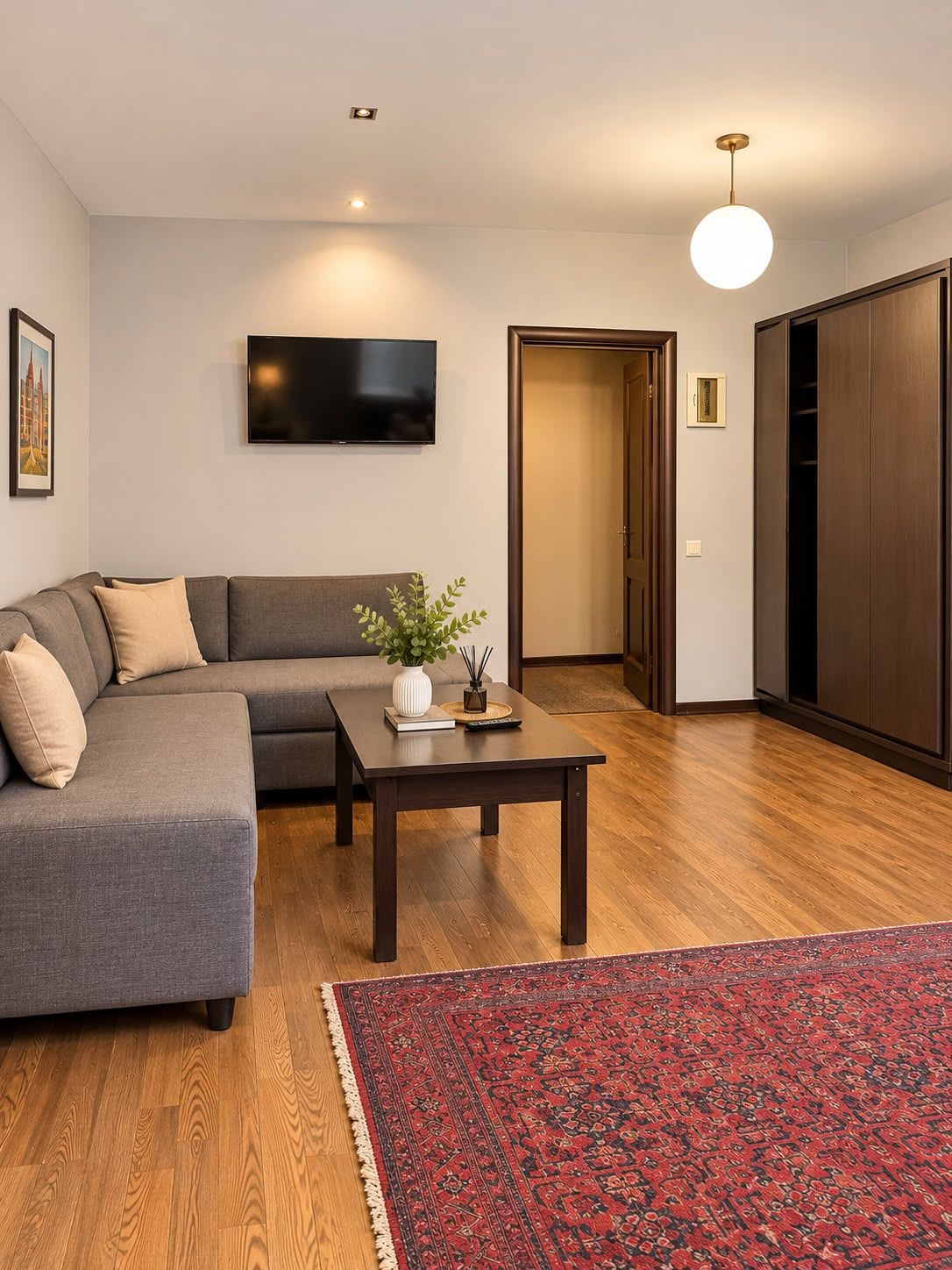 Een moderne woonkamer met een modulaire bank, een salontafel, een flatscreen televisie, een houten vloer en een rood tapijt met dessin.