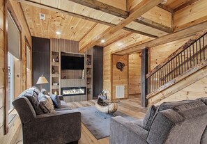 Ein gemütliches Blockhaus-Interieur mit Kamin, Holzwänden, einer Couch und einer Treppe.