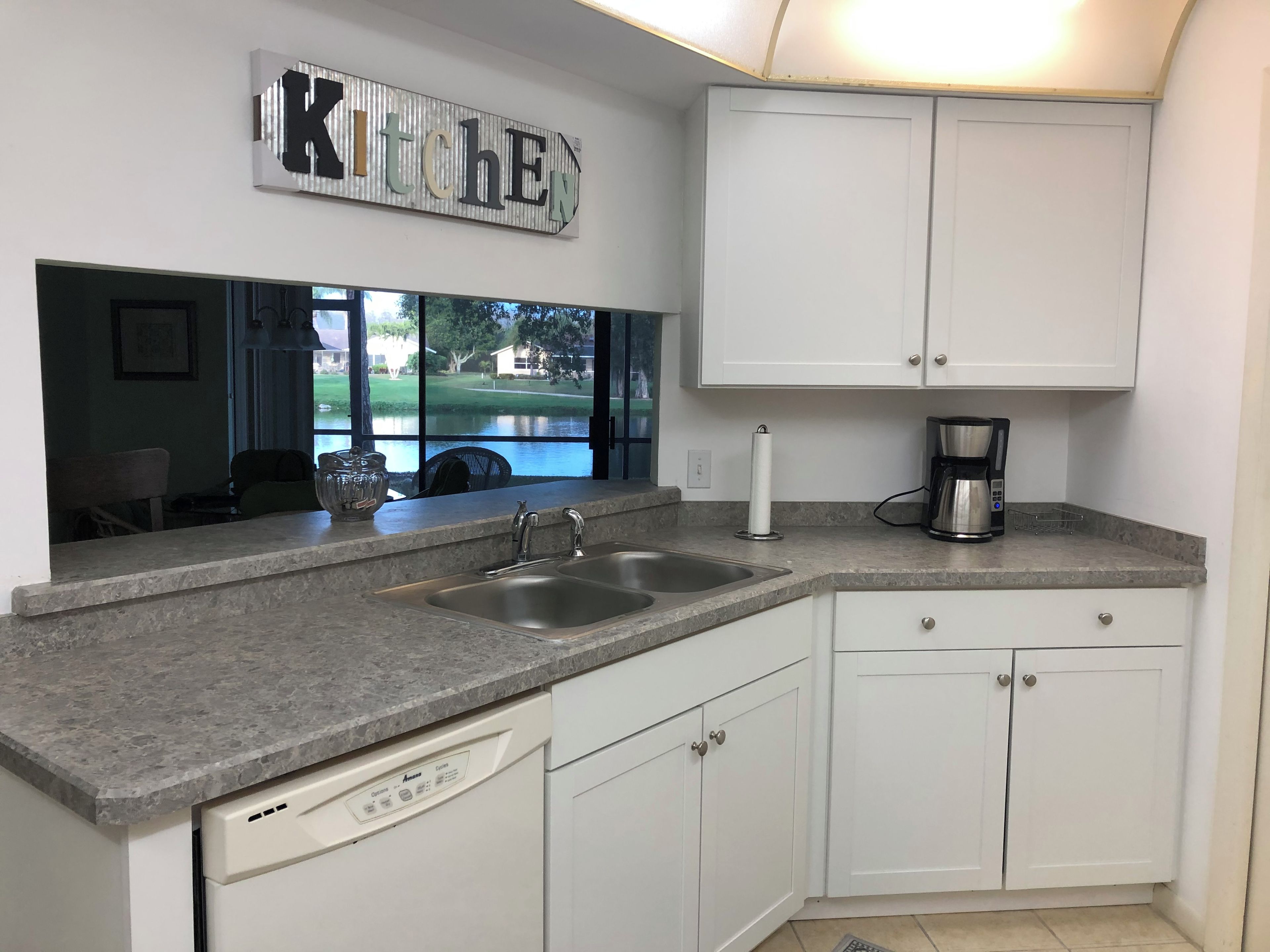 A kitchen with a double sink, white cabinets, a coffee maker, and a view of a golf course through the window.
