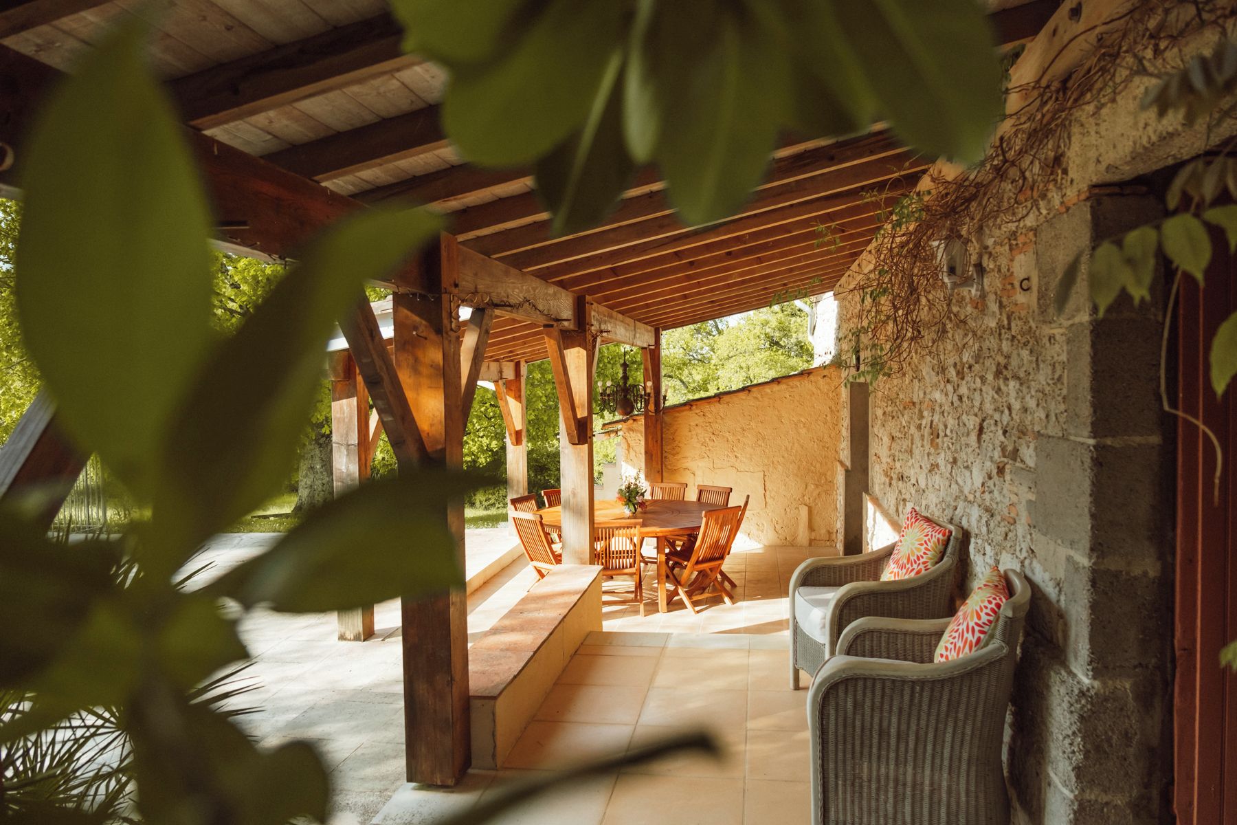 An outdoor patio with a wooden table and chairs, surrounded by stone walls and greenery.