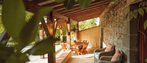 An outdoor patio with a wooden table and chairs, surrounded by stone walls and greenery.