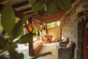An outdoor patio with a wooden table and chairs, surrounded by stone walls and greenery. - Gorgeous Family-Friendly Villa in Southwest France - Sleeps up to 10 (Mauvezin-sur-Gupie)