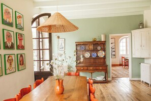 A dining area with a wooden table, chairs, a hanging light fixture, a wooden cabinet with dishes, and framed artwork on the wall. - Gorgeous Family-Friendly Villa in Southwest France - Sleeps up to 10 (Mauvezin-sur-Gupie)
