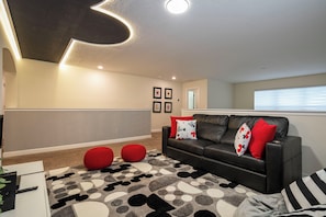 A living room with a black leather sofa, red and white patterned cushions, a grey and black patterned rug, and a ceiling with recessed lighting. - Near Disney 5BR Pool Home with Themed Kids Rooms (Kissimmee)