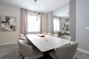 A modern dining room with a large table, chairs, and a painting on the wall. - Near Disney 5BR Pool Home with Themed Kids Rooms (Kissimmee)
