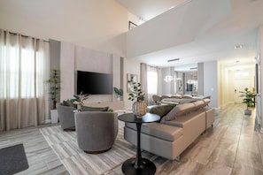 A modern living room with a flat-screen TV, grey sofas, a coffee table, and a potted plant. - Near Disney 5BR Pool Home with Themed Kids Rooms (Kissimmee)