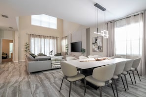 Una sala moderna con sofá, mesa de centro y televisor. Hay un comedor con mesa y sillas.