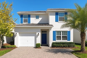 A two-story house with a white exterior, blue shutters, a garage, and a front entrance. - Near Disney 5BR Pool Home with Themed Kids Rooms (Kissimmee)